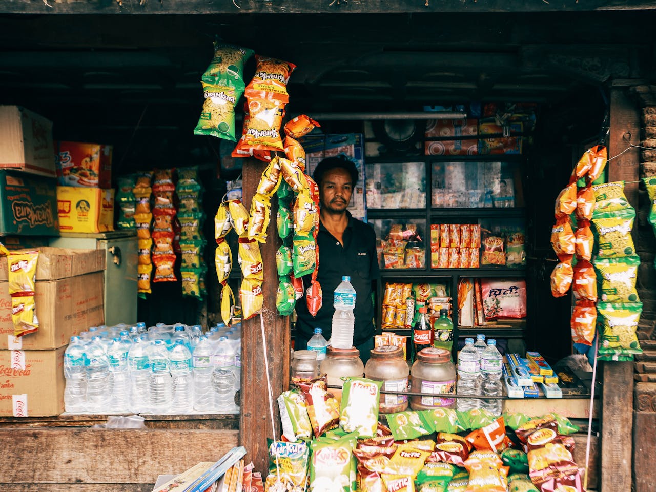 Image of a vendor in a vibrant local convenience store selling snacks and bottled water.